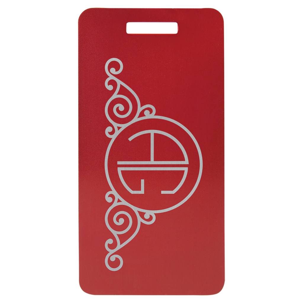 Red anodized aluminum luggage tag with decorative swirl design and circular monogram.