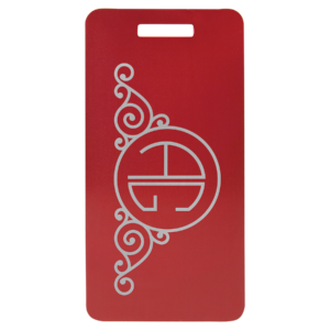 Red anodized aluminum luggage tag with decorative swirl design and circular monogram.