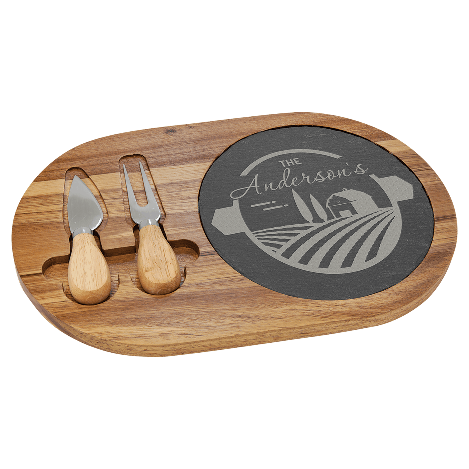Acacia wood and slate oval cheese board set with engraved farm design and two stainless steel cheese tools on a transparent background.